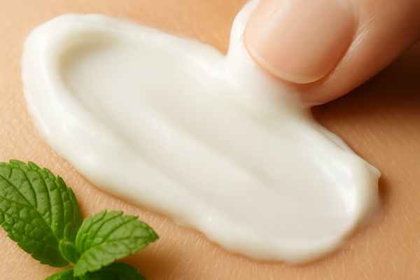 Macro close-up of CBD cream being smoothed onto skin with mint leaves in foreground