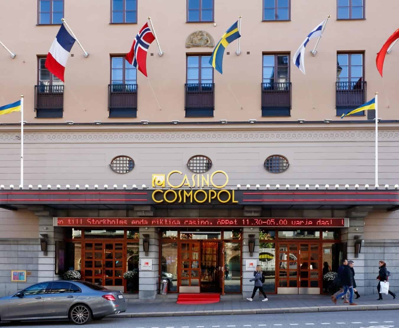 Exterior of Casino Cosmopol in Stockholm with Swedish and international flags above the entrance and people walking by.