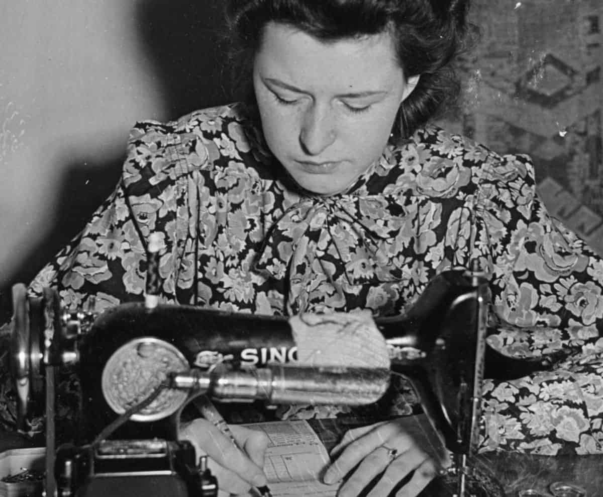 Undated archive photograph of a woman at a sewing machine with betting slips on the desk.