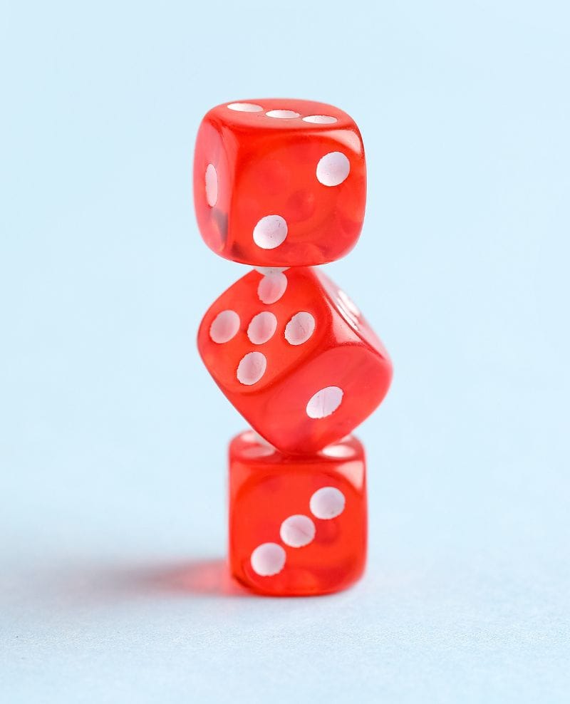 Three red dice stacked in an unstable tower, illustrating calculated risk in iGaming.