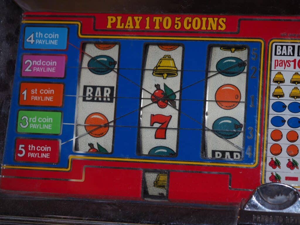 Close-up of fruit, bell and BAR symbols on the reels of an older slot machine.