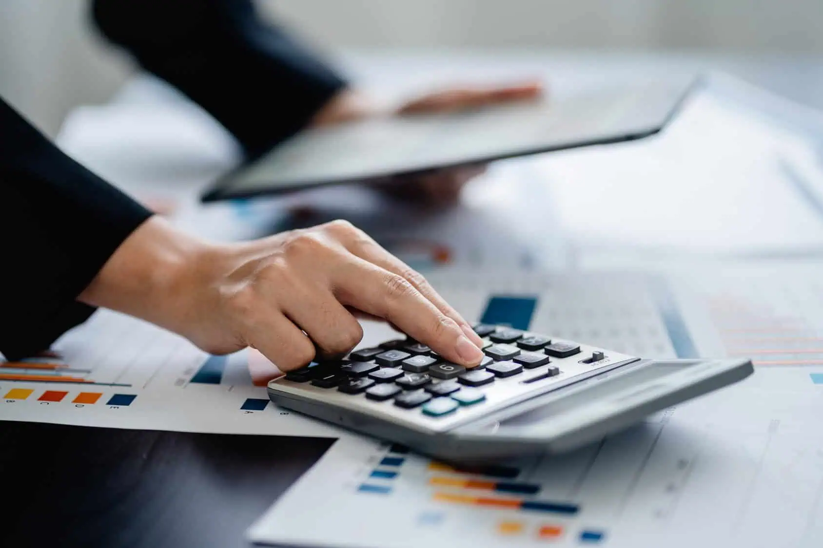 An accountant using a calculator beside financial documents and a tablet.
