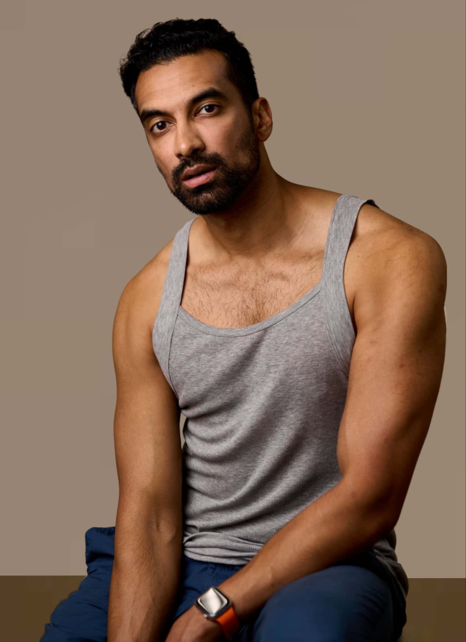 Maaz Ali in a gray tank top, sitting in a photoshoot.