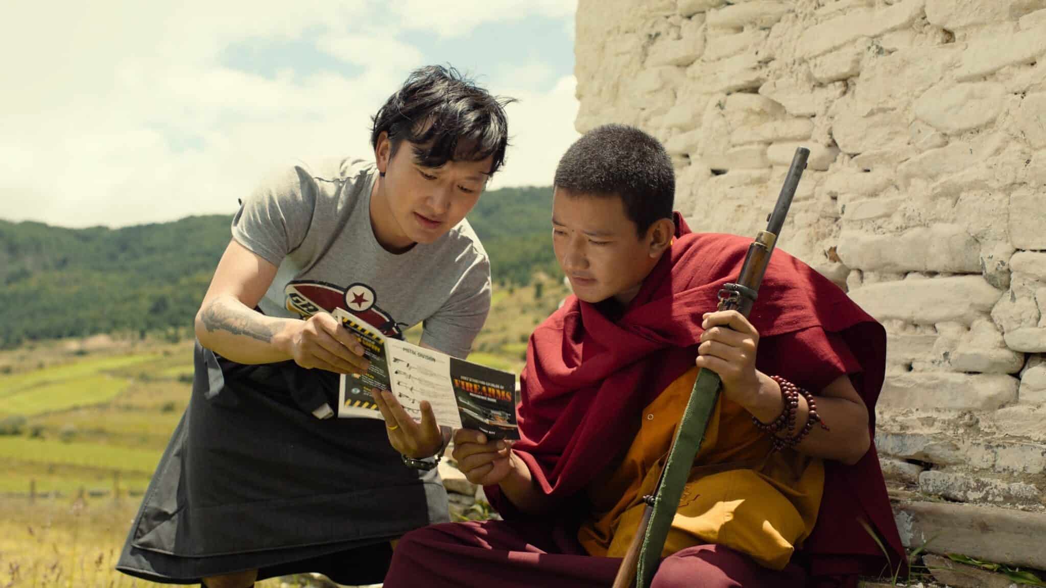 An Asian man is showing a pamphlet labeled "Firearms" to a monk who is holding gun.