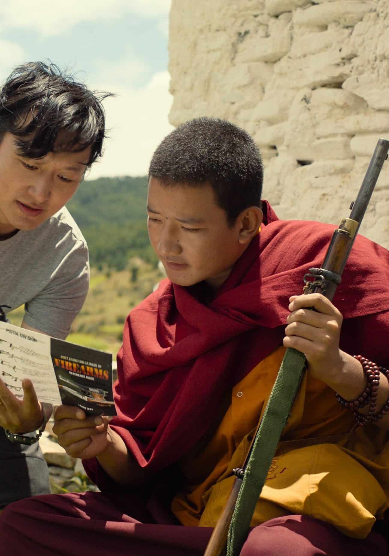 An Asian man is showing a pamphlet labeled "Firearms" to a monk who is holding gun.