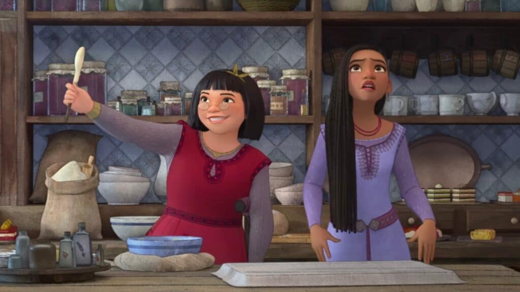 In the kitchen, an Asian girl with glasses and a bob cut excitedly gestures with a spoon to the left, while a taller dark-skinned woman with long braids looks exasperated to the right.