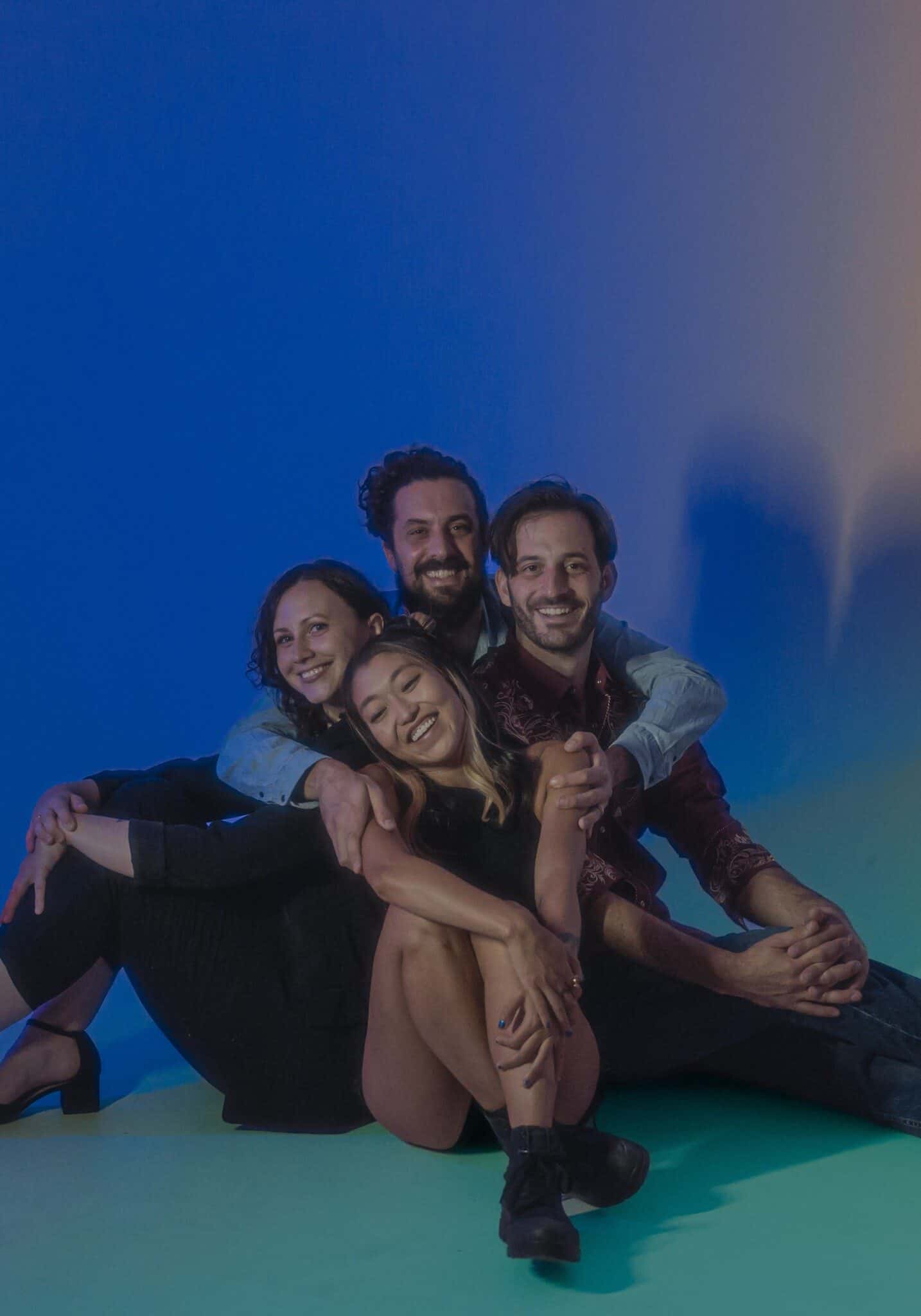 Four smiling people sit huddled together in a hug.