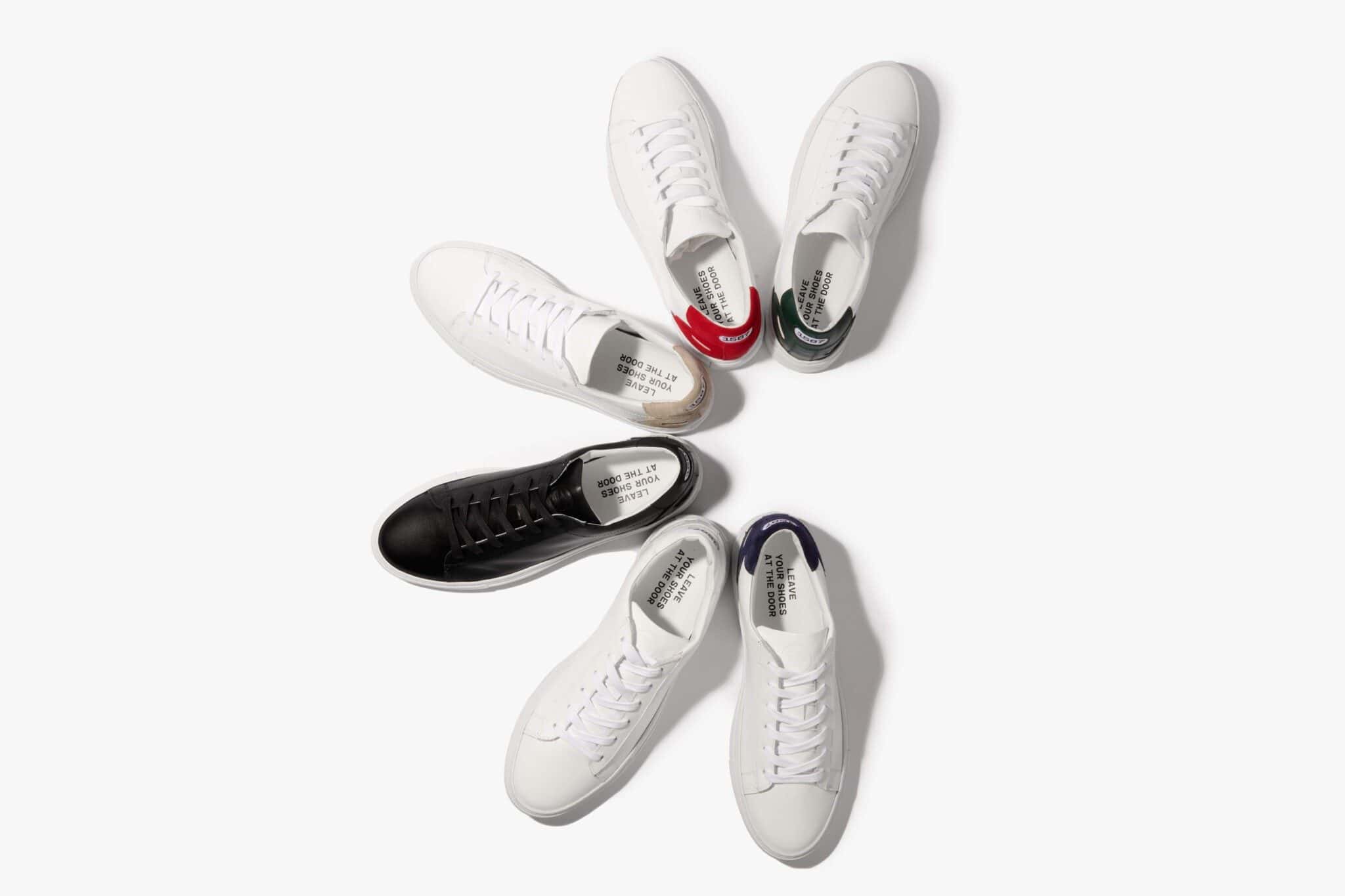 Five white sneakers and one black sneaker form a semi-circle shape, against a white backdrop.