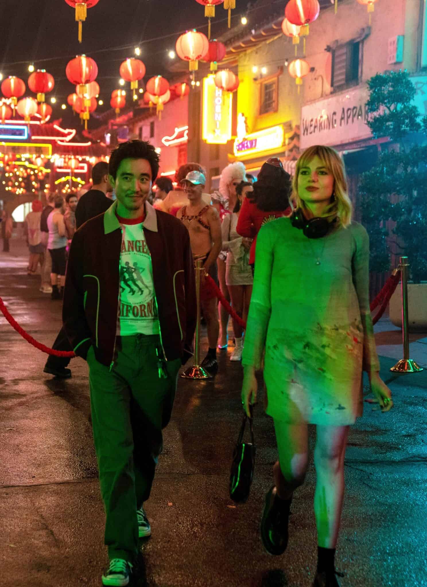 Justin H. Min and Lucy Boynton in "The Greatest Hits" walk on a city street with shops and red lanterns in the background.