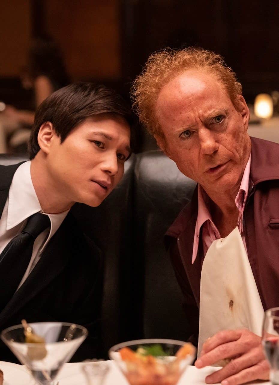 Hoa Xuande and Robert Downey Jr. in "The Sympathizer," with a restaurant and diners in the background.