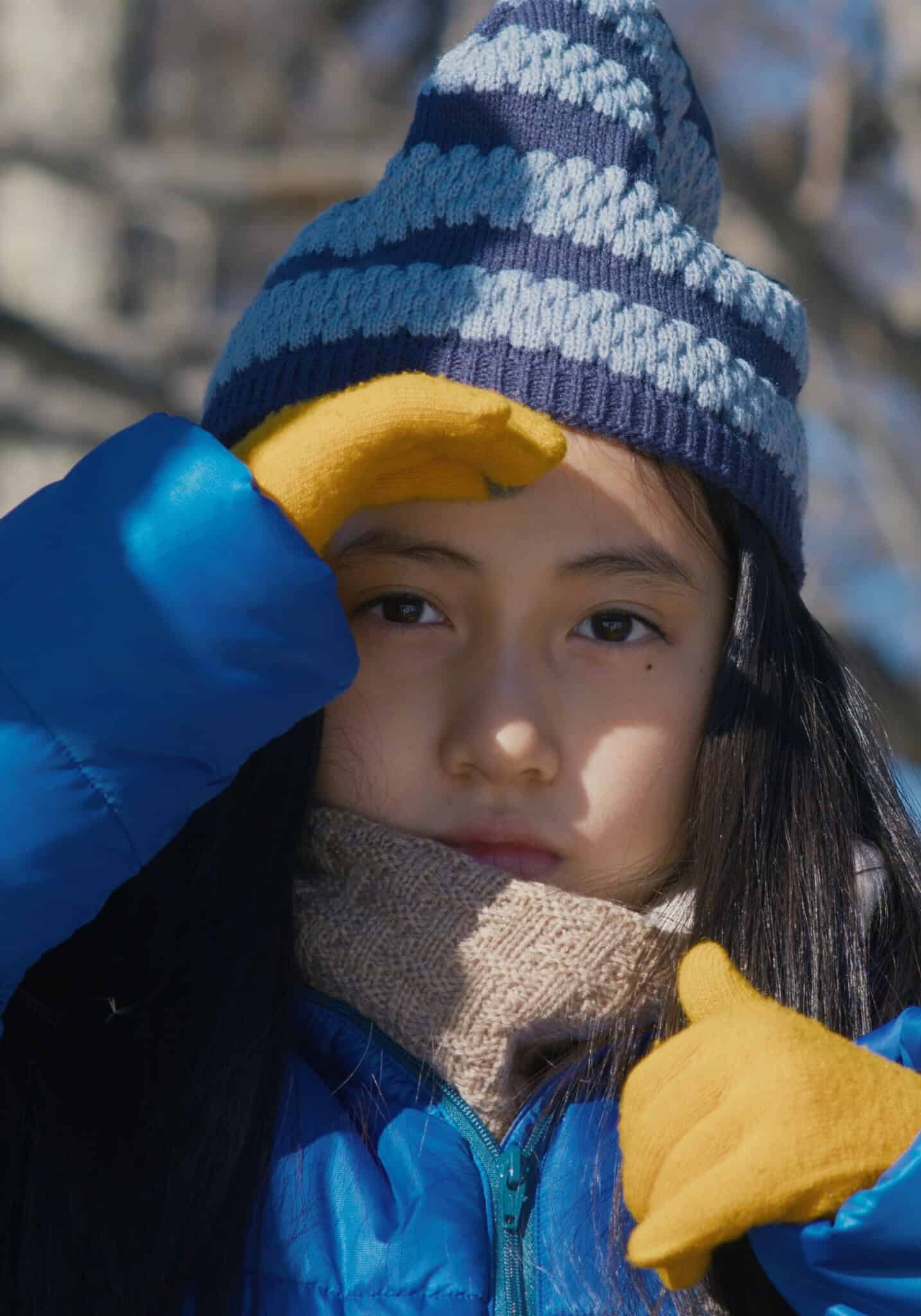 Young girl cups hand over eyes and gazes into the camera.