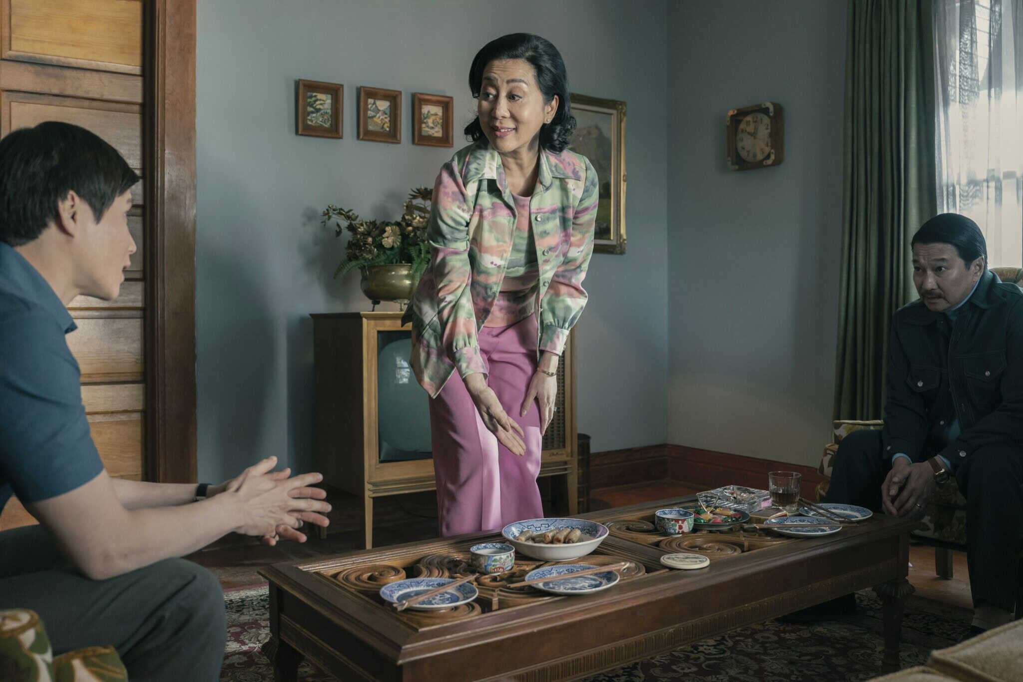 Vietnamese American actress Nguyen Cao Ky Duyen stands at a coffee table with food on top, bookended by actors Hoa Xuande and Toan Le, in "The Sympathizer."
