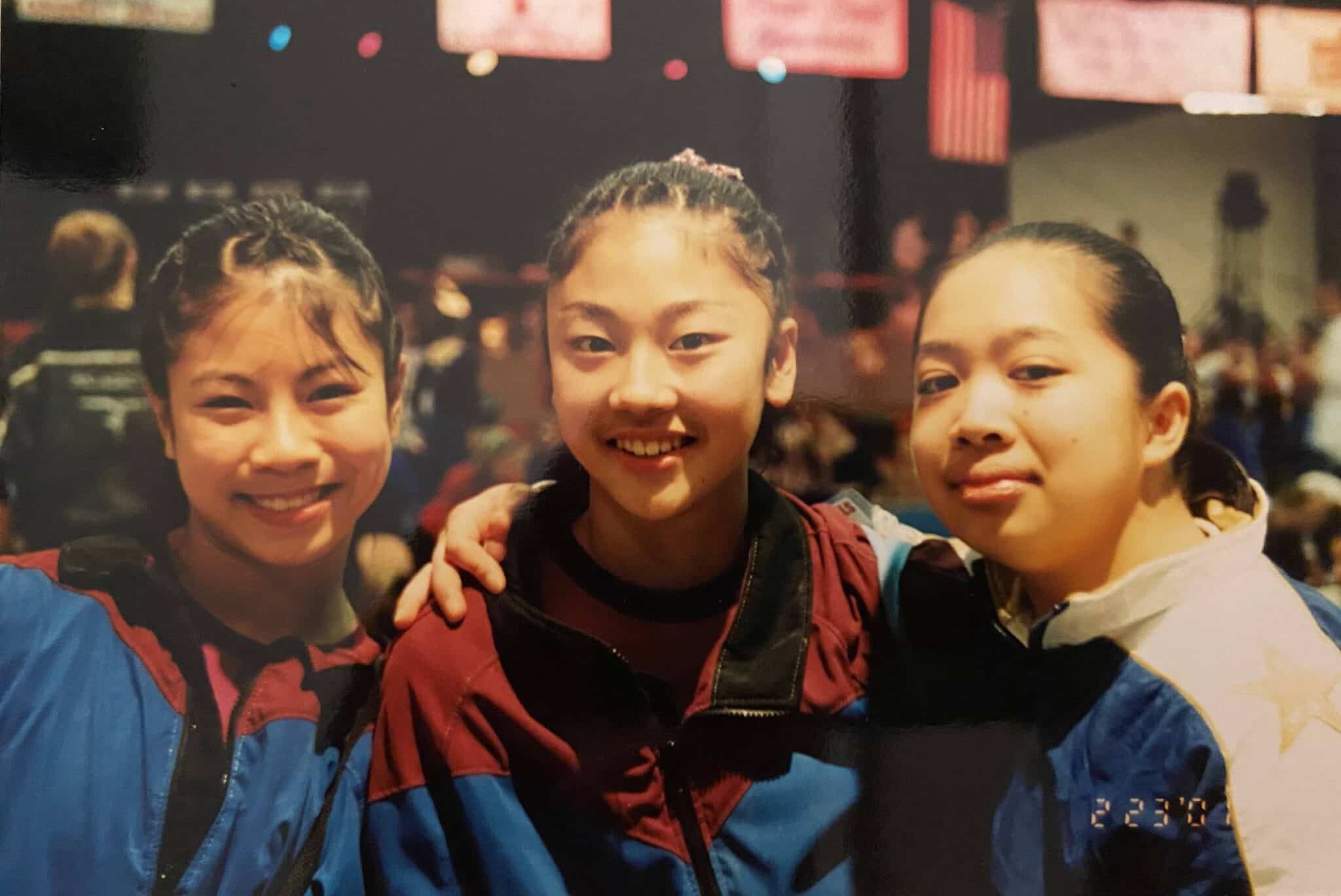 Three young Asian women stand together in blue and purple and blue and white jackets.