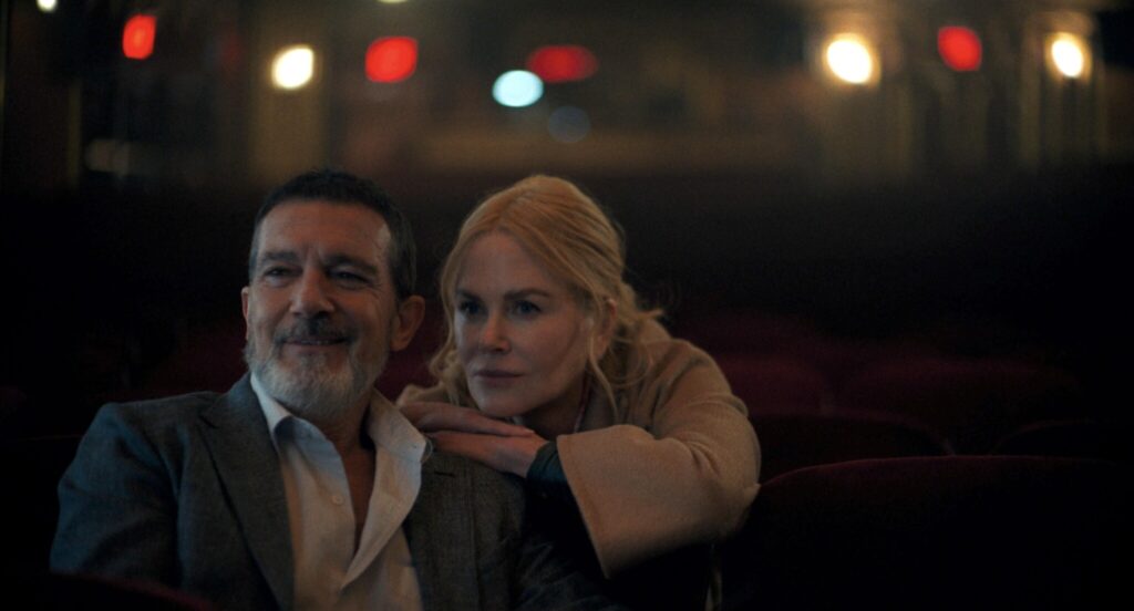 Still frame from "Babygirl." A man and women look off-screen while the woman rests both of her hands intimately on the man's shoulder, her head on top of her hands.