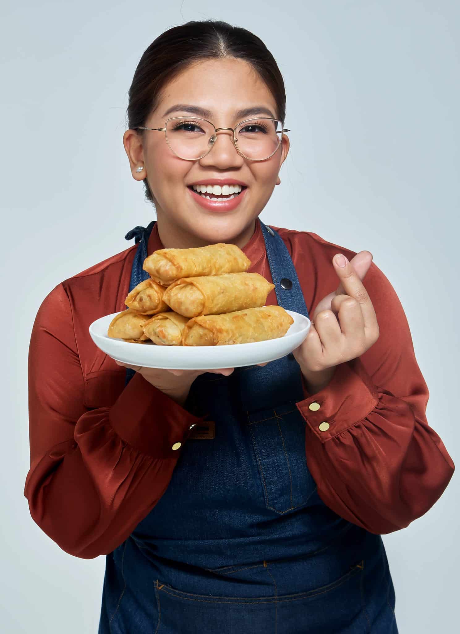 Abi Marquez holding a plate of lumpia with one hand and forming a heart with the other.