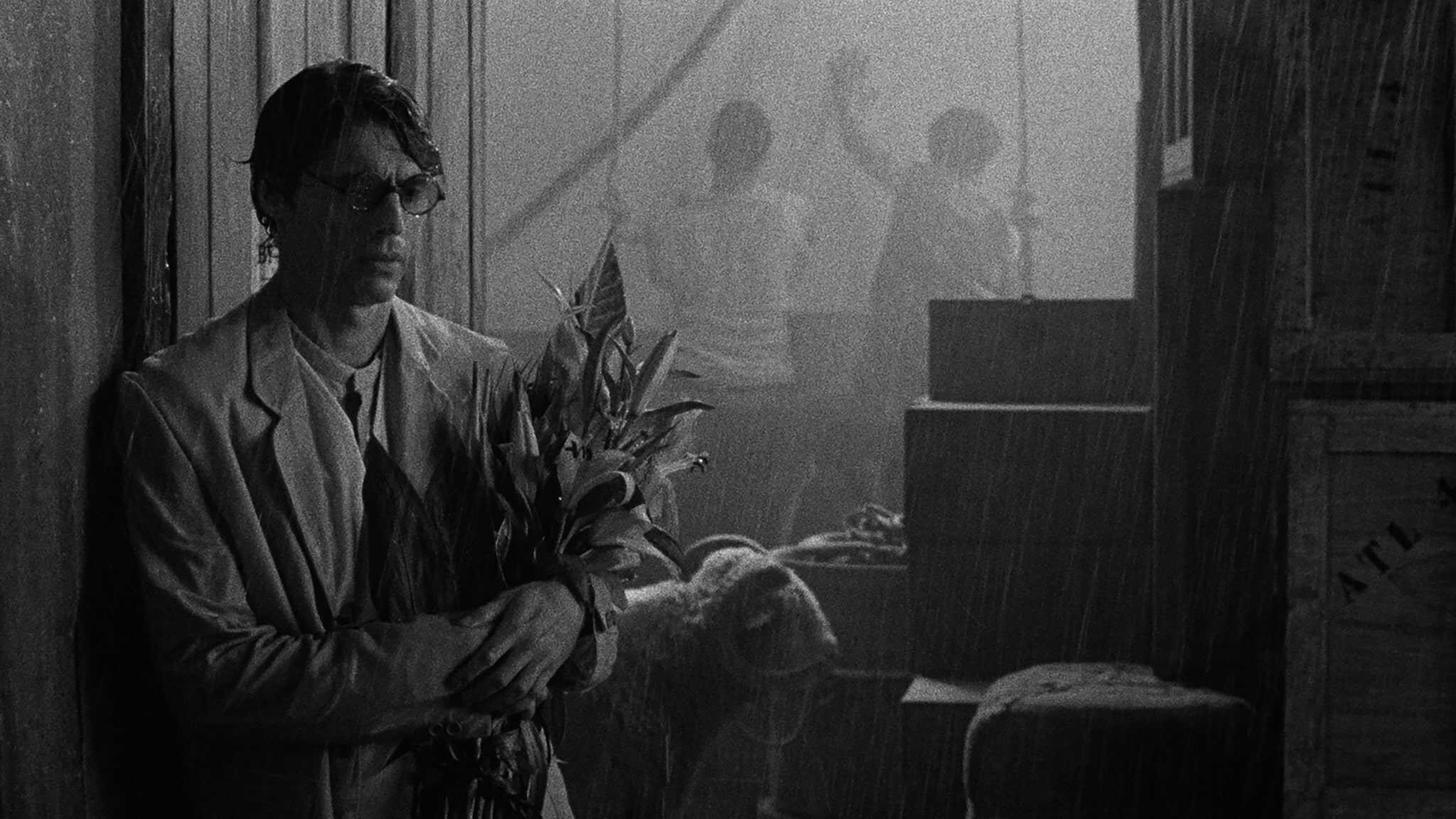 Still frame from "Grand Tour." A man holds flowers while standing in the rain.