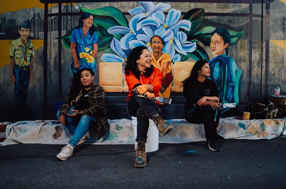 Three women sitting in front of a mural.