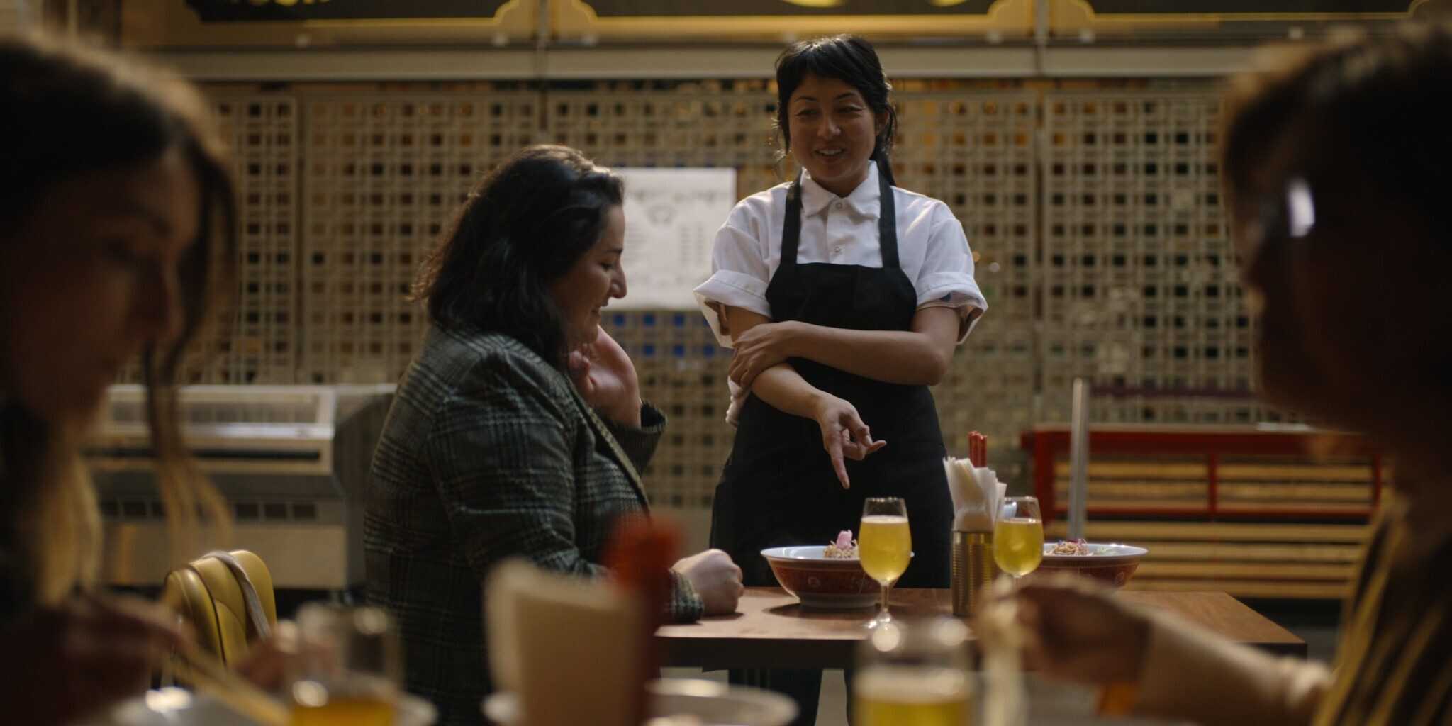 Nite Yun talking to a diner while pointing at a bowl of soup on the table in front of them.