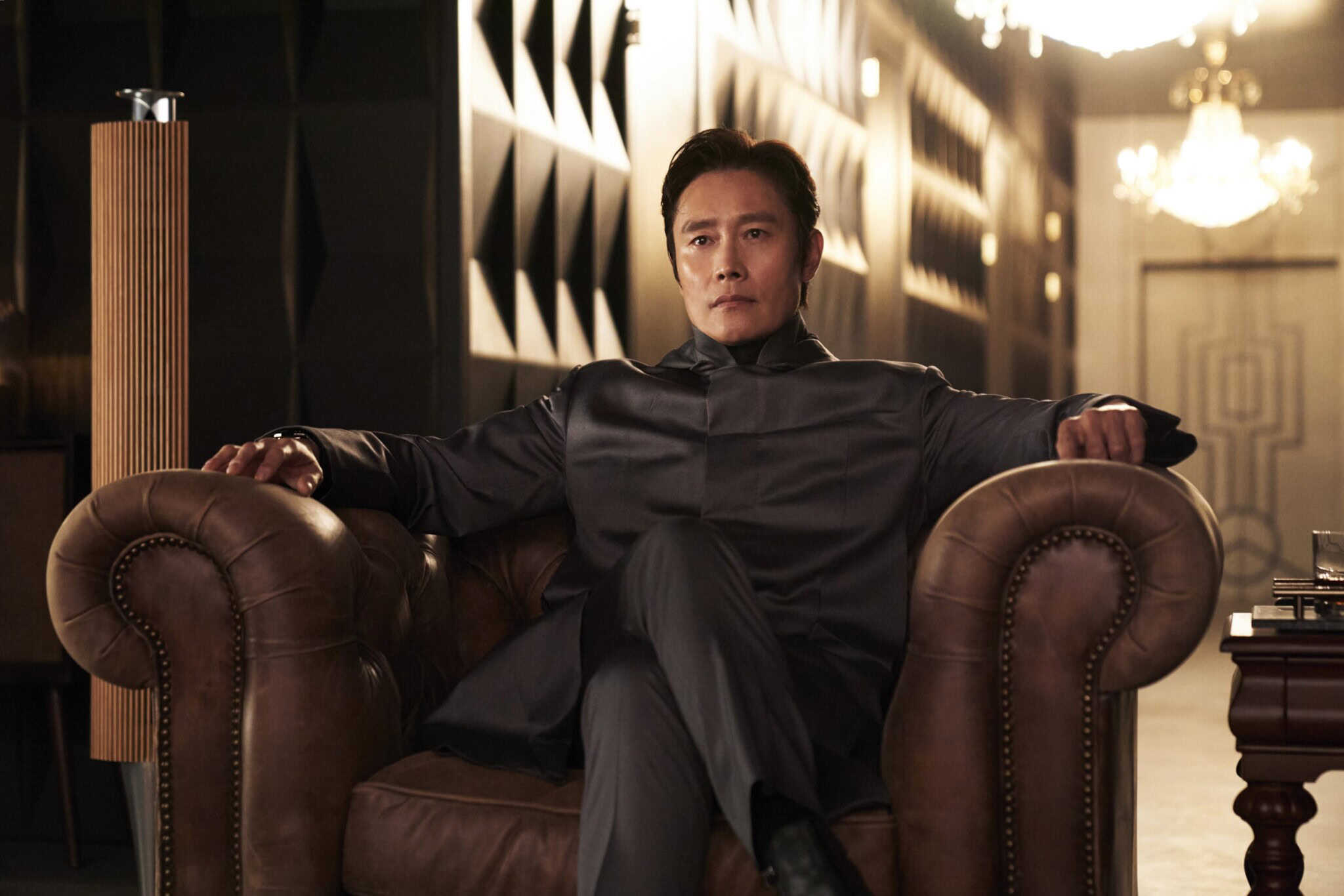 Lee Byung-hun as Hwang In-ho sitting in an armchair wearing all black.