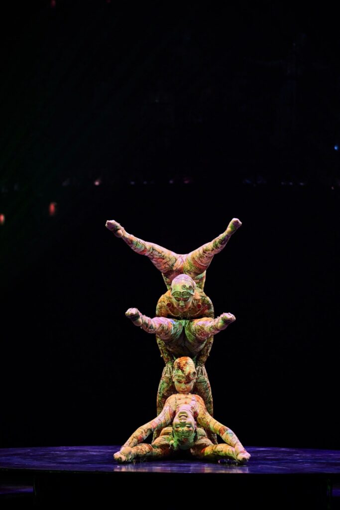 Three contortionists on stage during a performance balancing on top of each other.