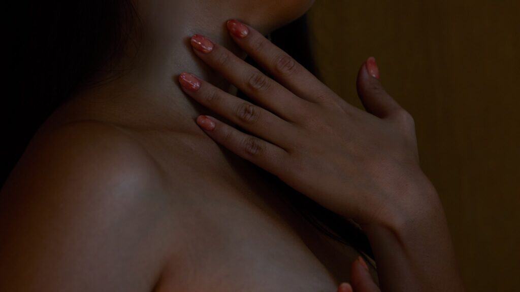 A woman touches her own neck sensually.
