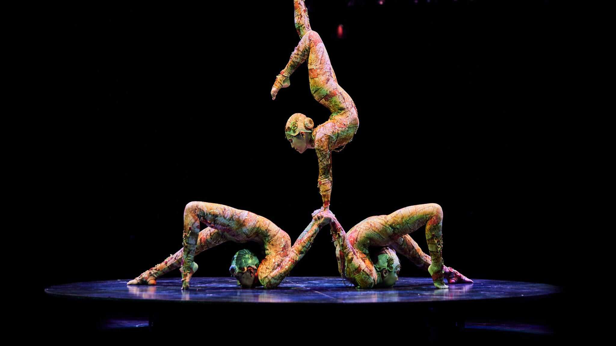 Three contortionists on stage, one balancing on top of the others.