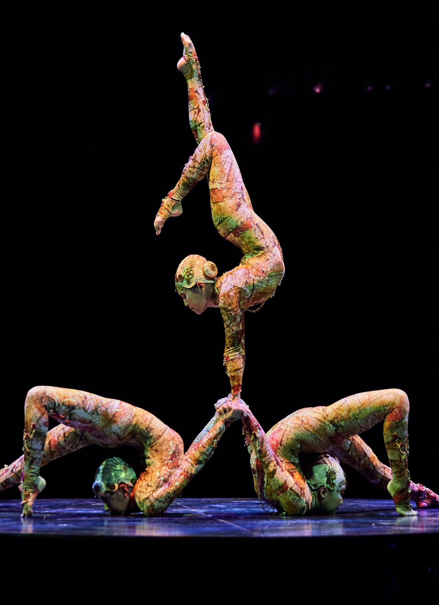Three contortionists on stage, one balancing on top of the others.