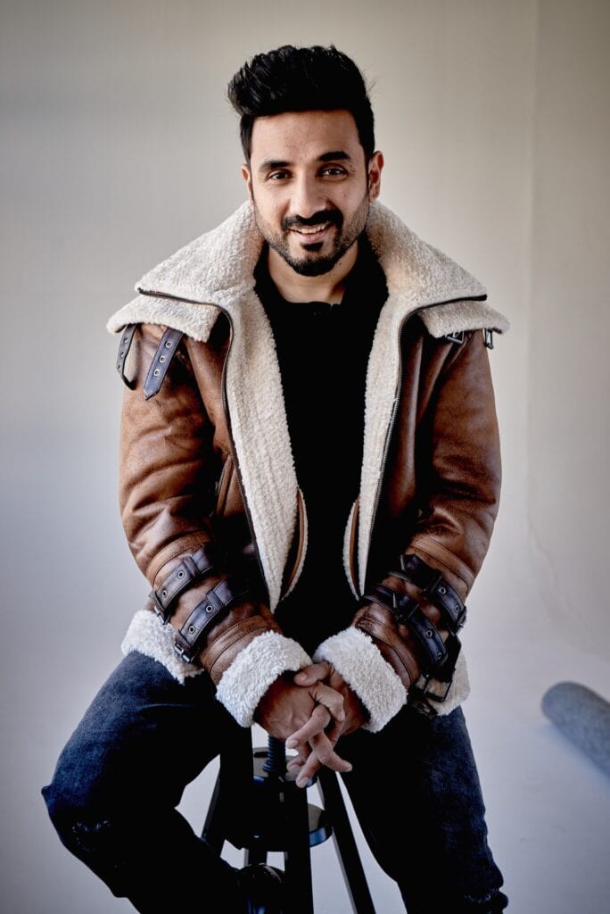 Vir Das sitting on a stool, smiling for the camera.