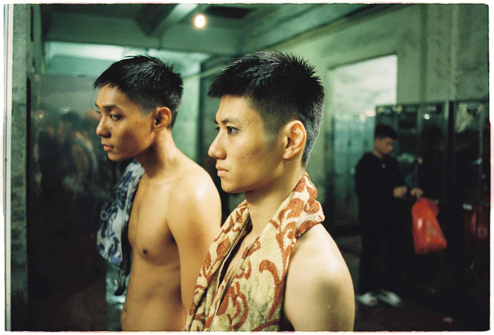 Still from "Viet and Nam"; two men stand shirtless in a locker room.