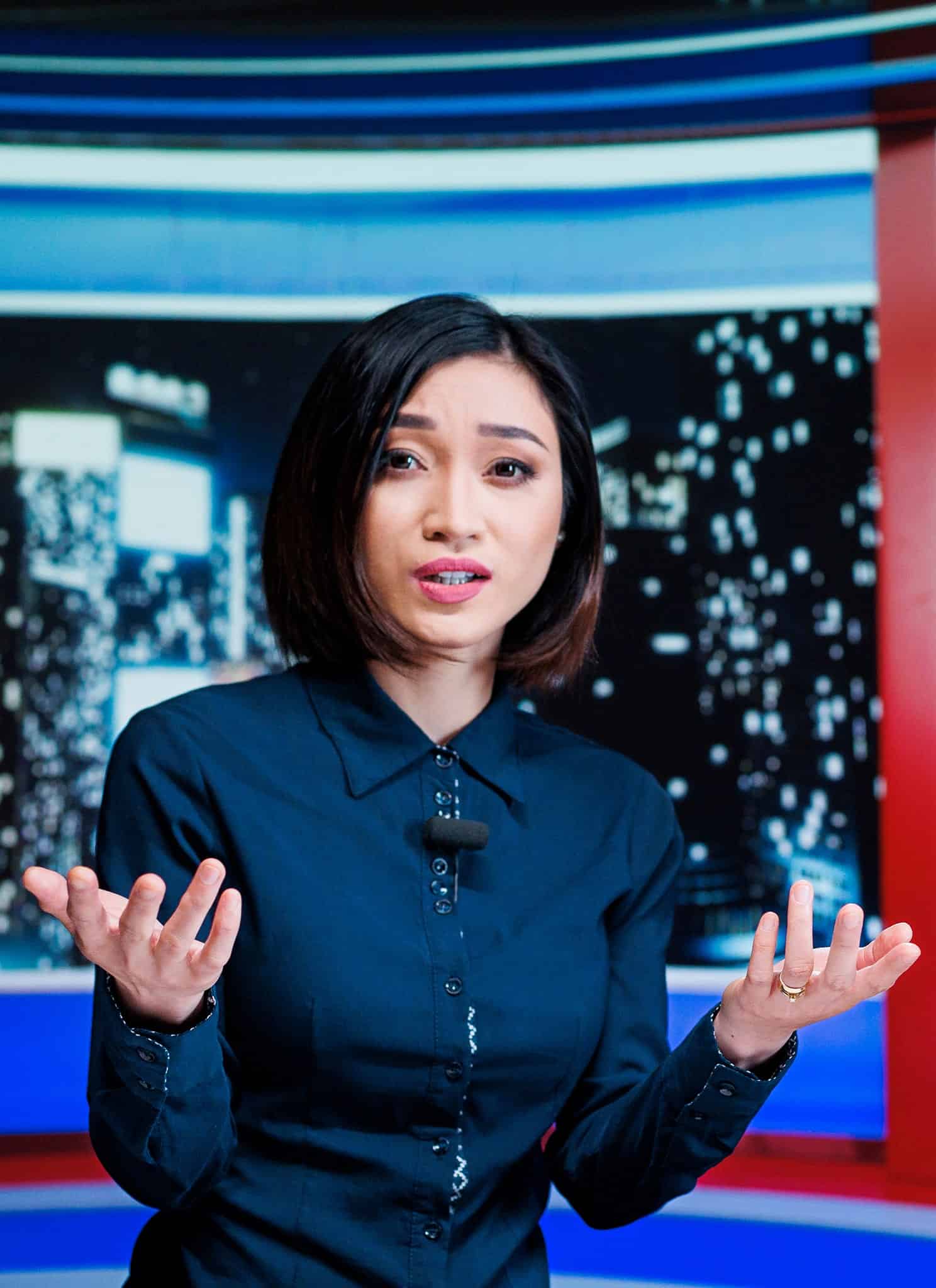 An Asian woman and a Black man speaking behind a news desk.