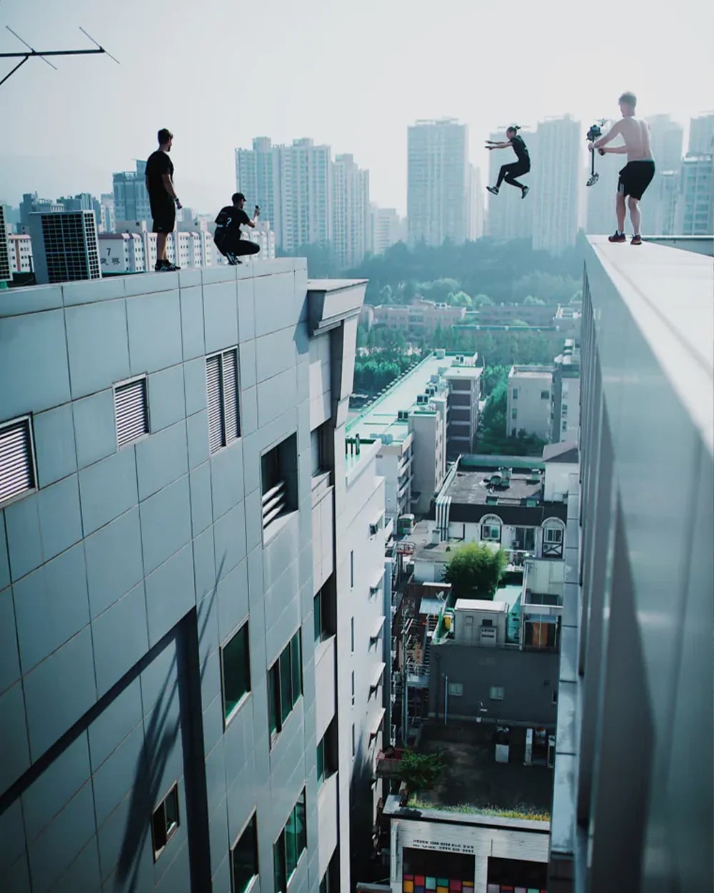 A man jumping between buildings while others record.