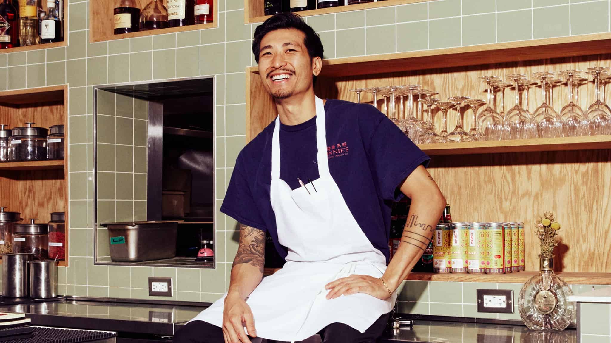 Chef Calvin Eng sitting on the counter of a kitchen and smiling.