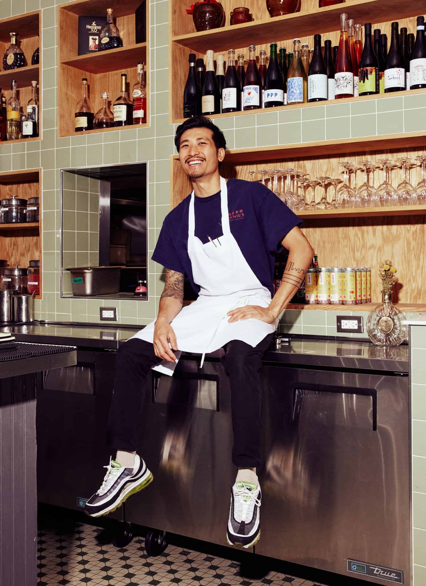 Chef Calvin Eng sitting on the counter of a kitchen and smiling.