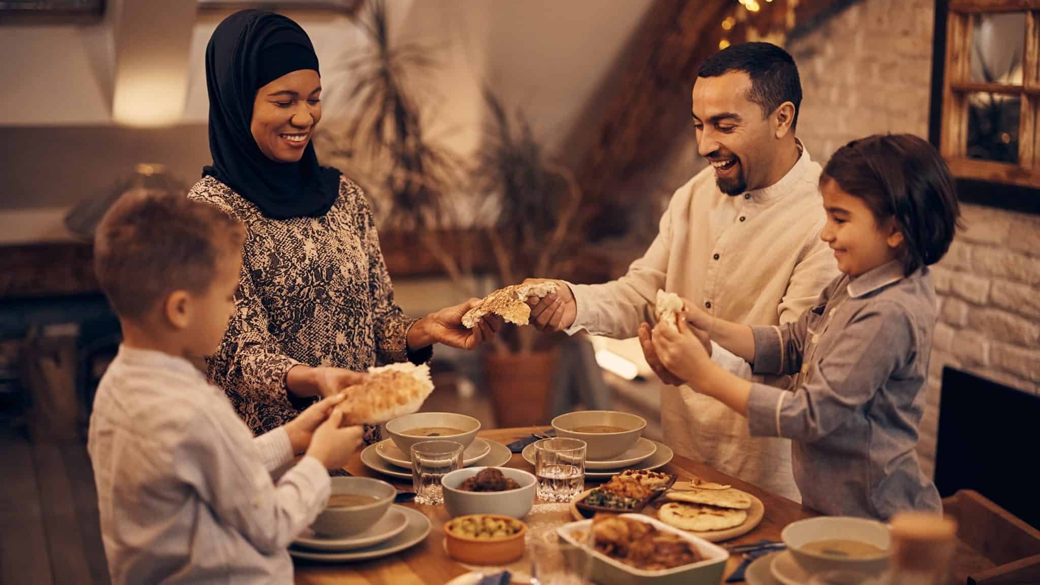 Happy Muslim parents and their kids sharing pita bread.