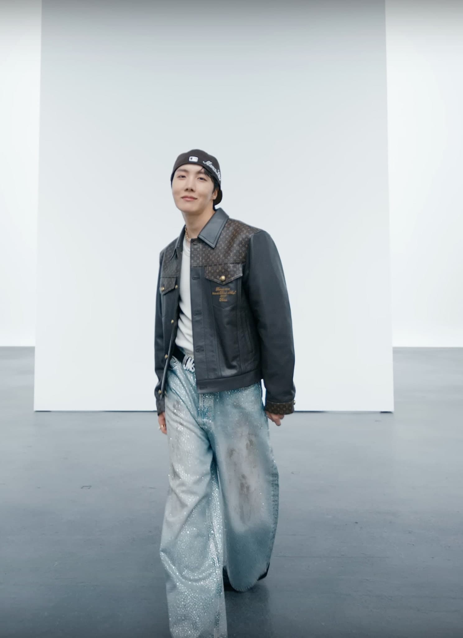 BTS' J-Hope standing in front of blank white canvas in a leather jacket.