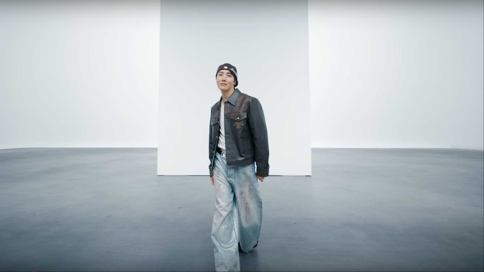BTS' J-Hope standing in front of blank white canvas in a leather jacket.
