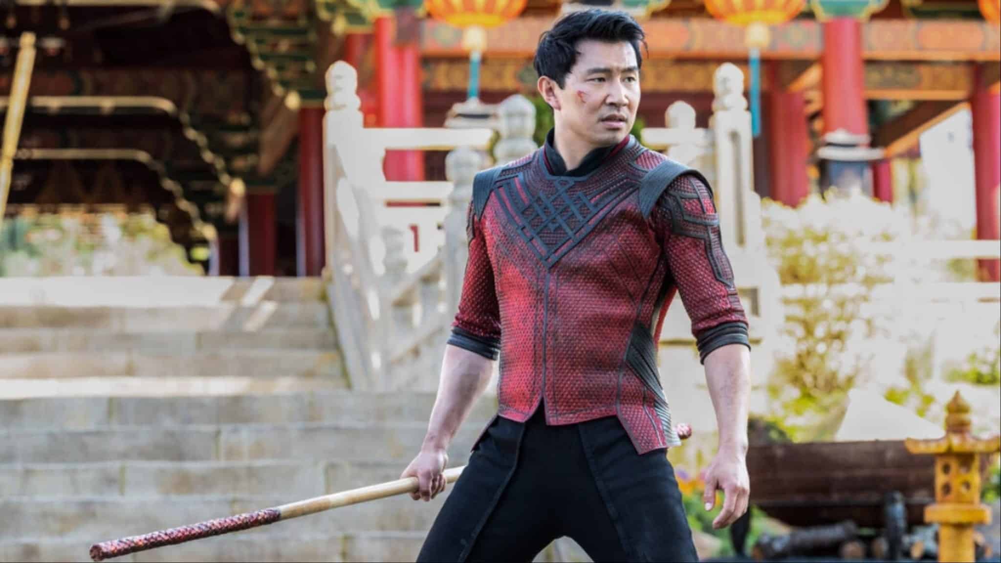 Simu Liu as Shang-Chi in red outfit and black pants holding a stick