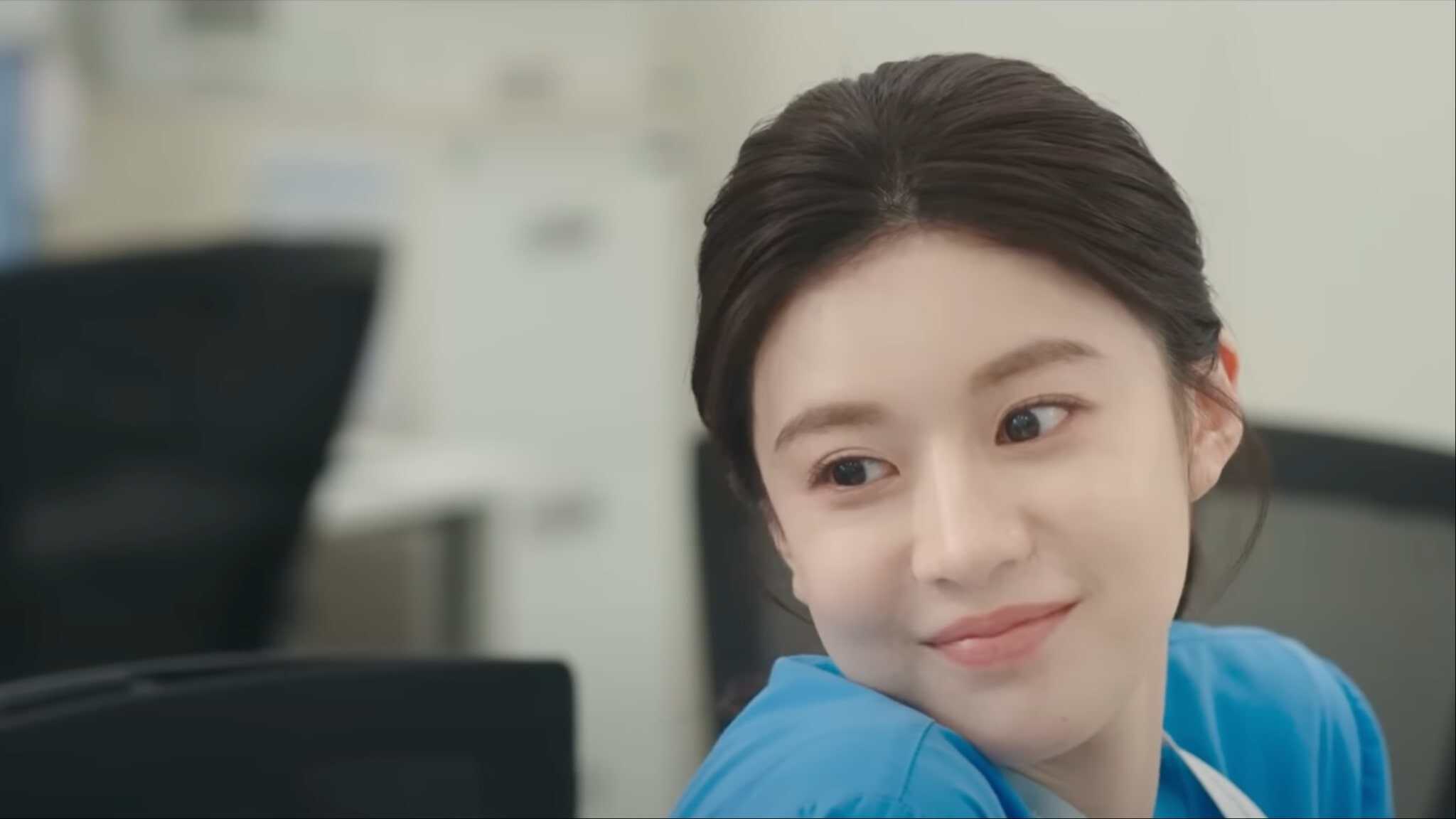 Go Youn Jung in blue scrubs sitting in chair.
