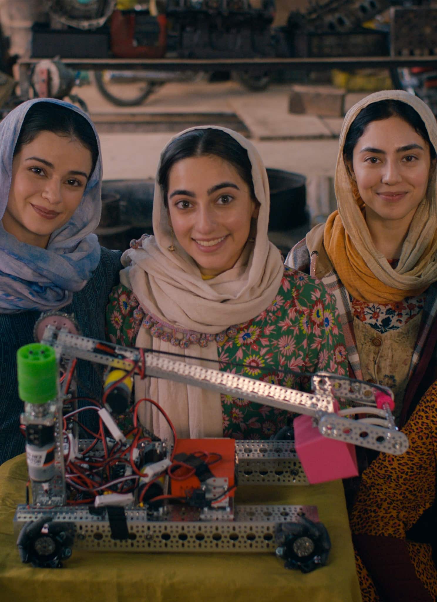 A group of women and a man smile at the camera, posing behind a small robot.