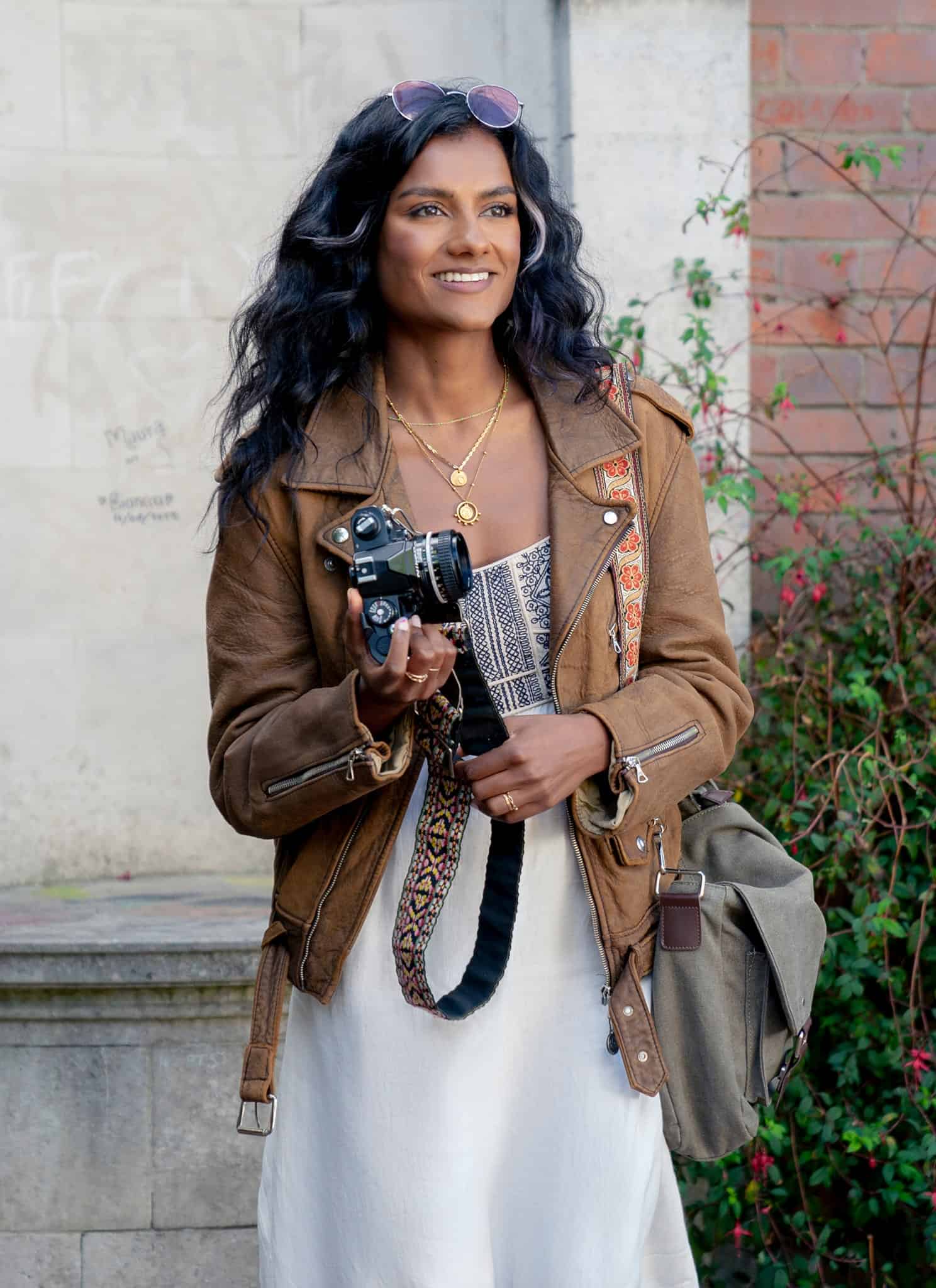 Simone Ashley in a brown jacket and white dress as Pia in "Picture This."