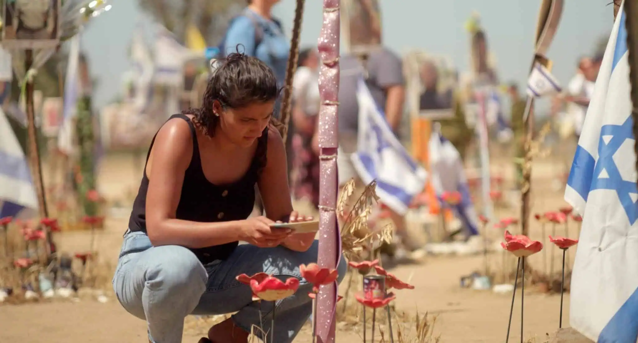 Still from "October 8" film; a woman squats on the ground looking at a paper in her hands.