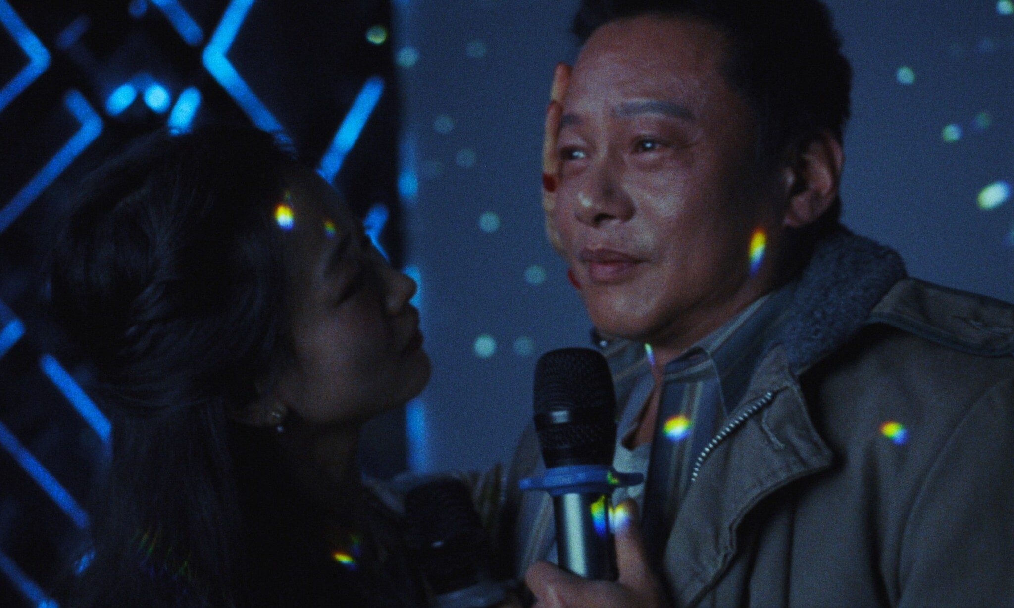 Still from "Blue Sun Palace"; two people holding a mic embracing each other.
