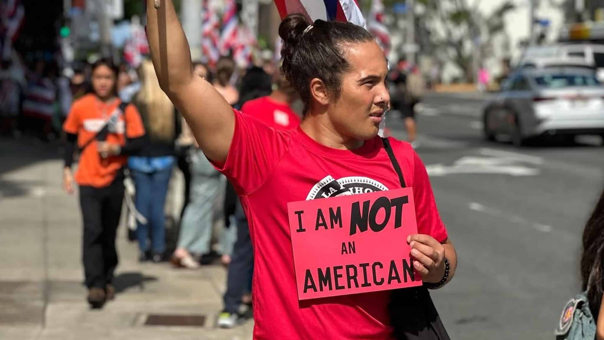 A Native Hawaiian holding a sign that says "I AM NOT AN AMERICAN."