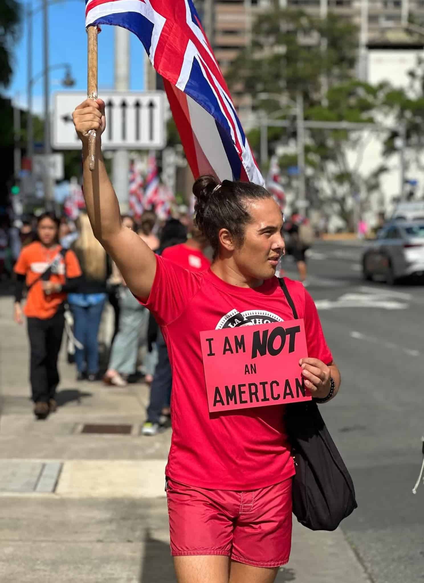 A Native Hawaiian holding a sign that says "I AM NOT AN AMERICAN."