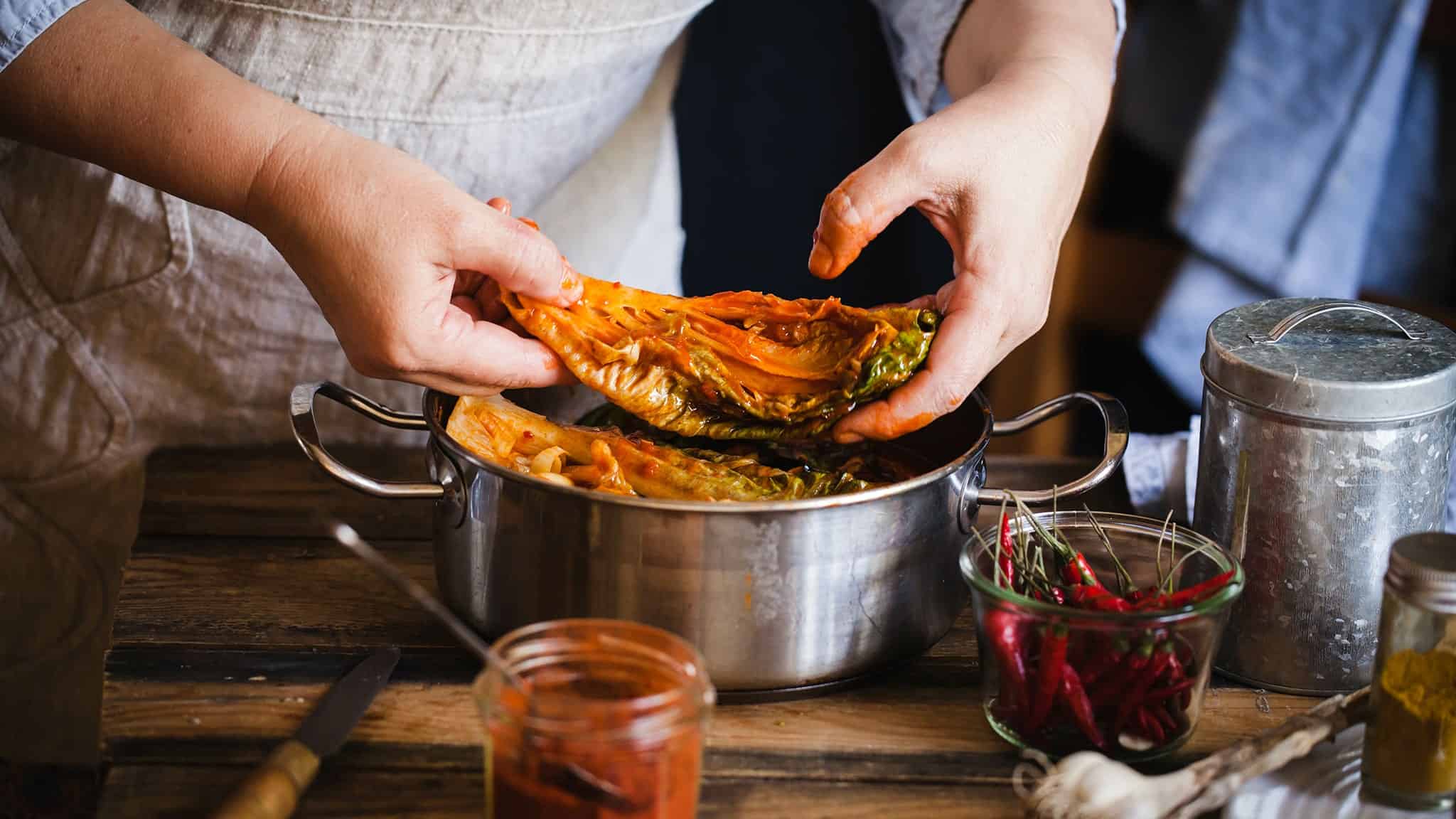 Some placing kimchi into a pot.