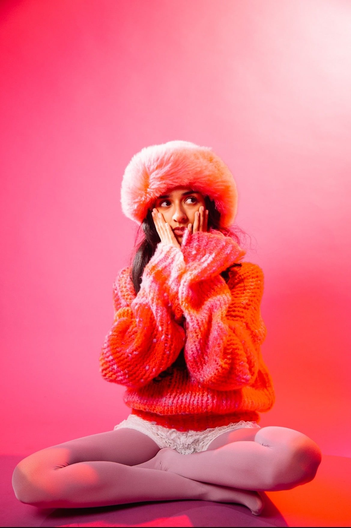 Misha Sattar in a red and orange outfit, posing with her hands on her cheeks.