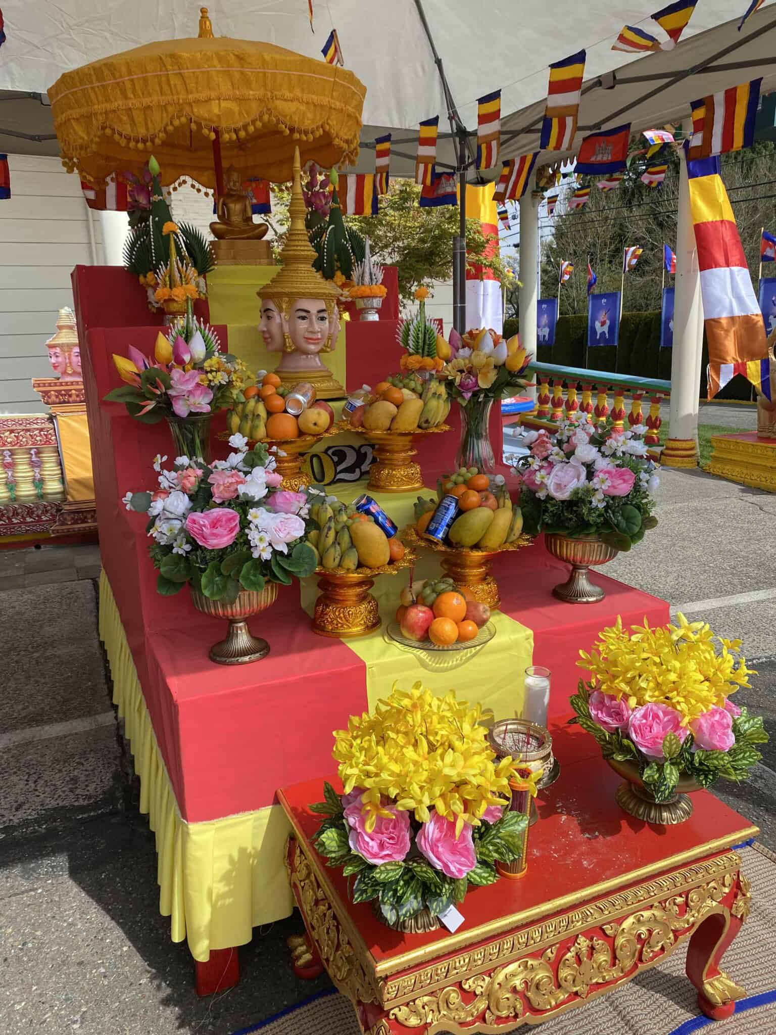An altar with fruit and flowers, with small colorful flags in the background.