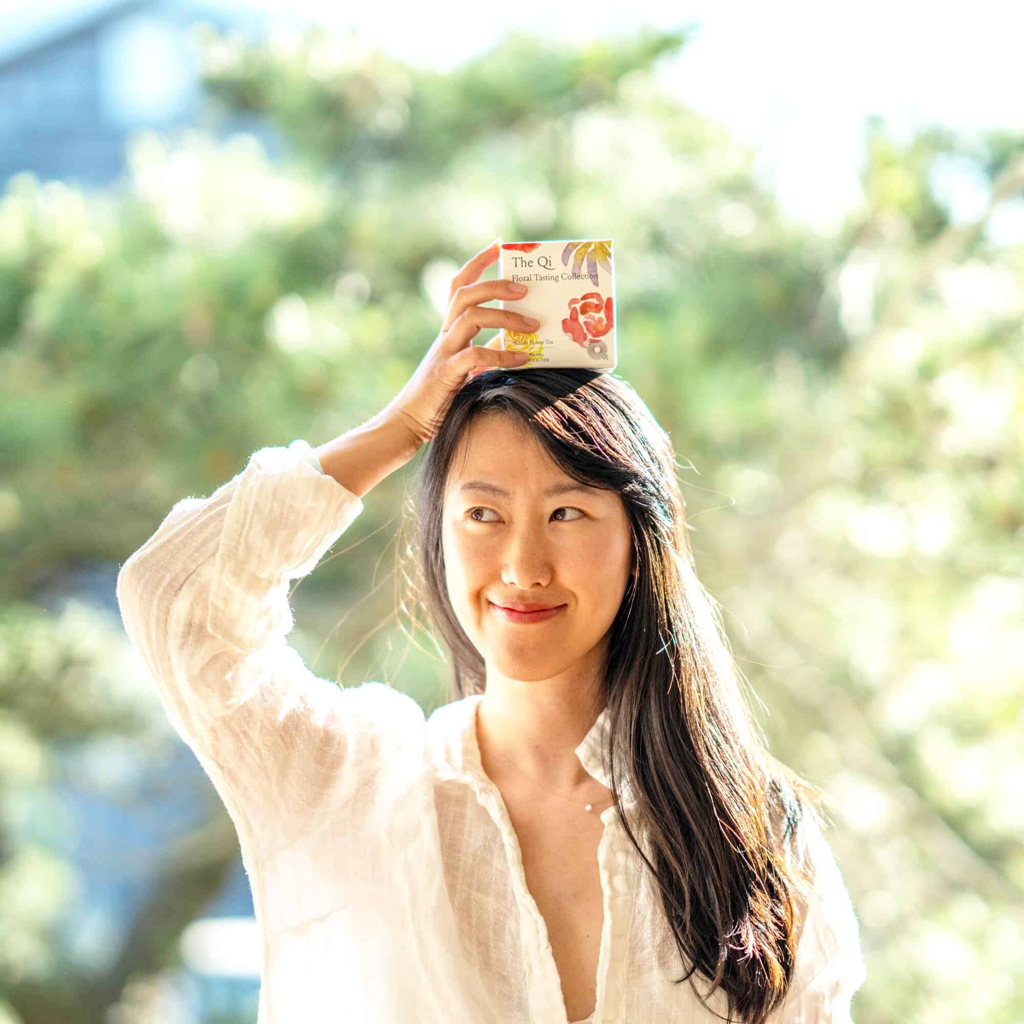 Lisa Li smiling and holding a box of her product on her head.