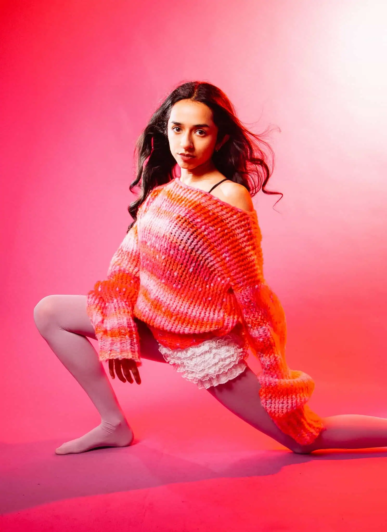 Misha Sattar posing in front of a pink background wearing a pink and orange outfit.