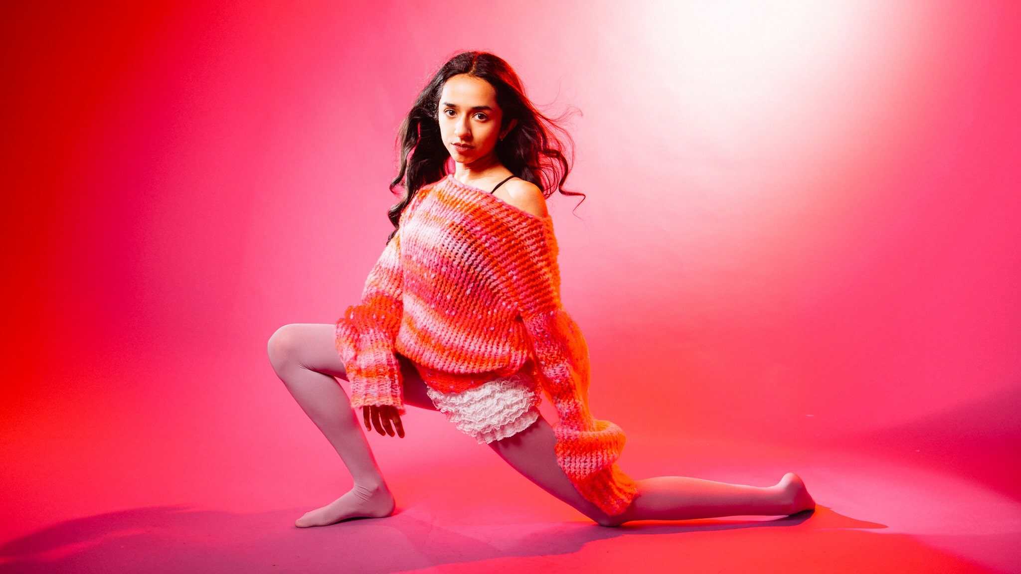 Misha Sattar posing in front of a pink background wearing a pink and orange outfit.